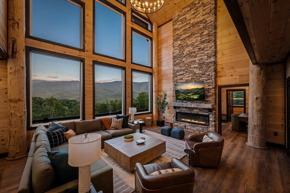 Two story great room with stacked stone fireplace and mountain view glass at dusk, custom Gatlinburg lodge