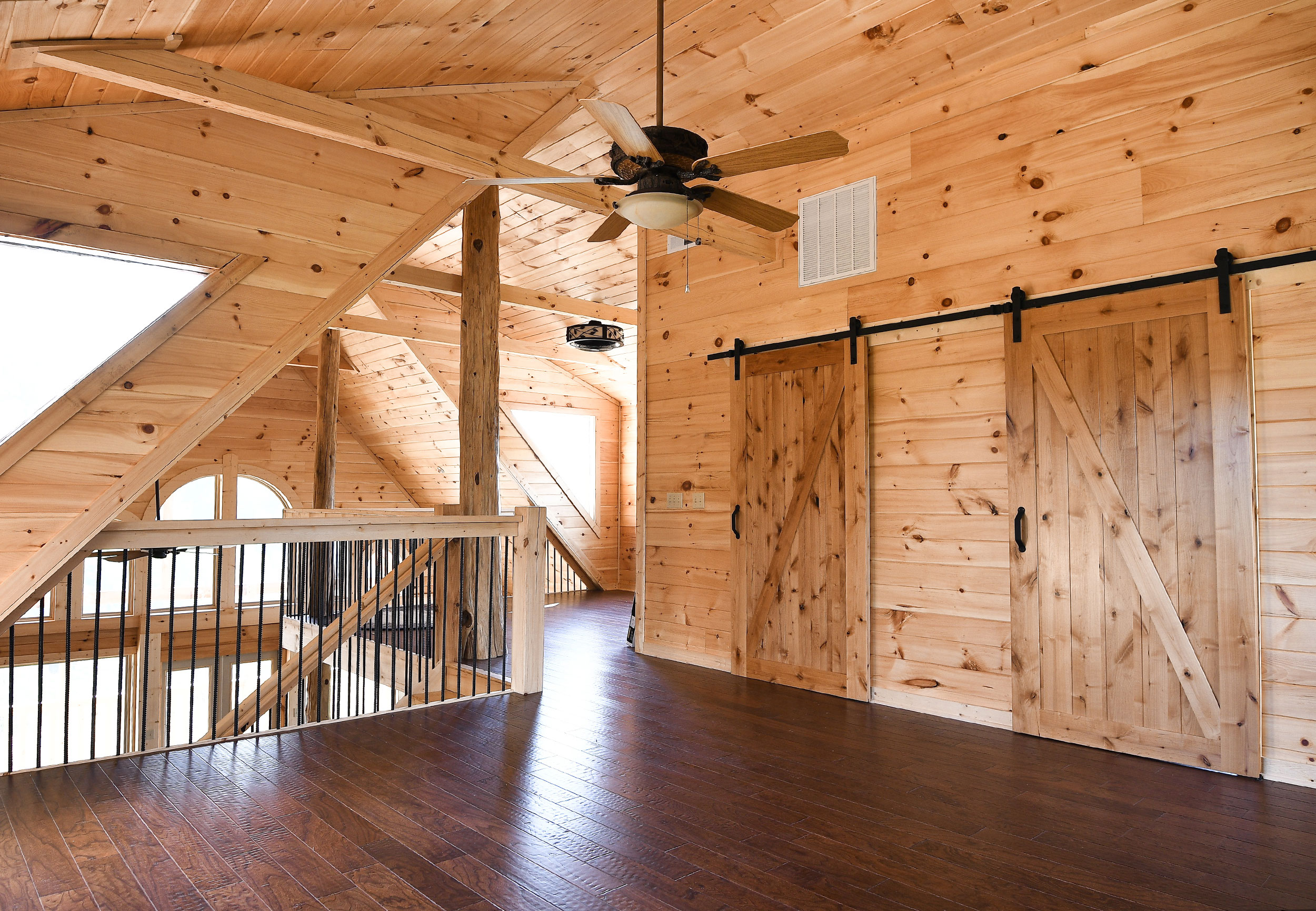 Cabin loft interior, tongue-and-groove pine ceiling, barn sliding doors, dark hardwood floors, and open staircase at Laurel Estates