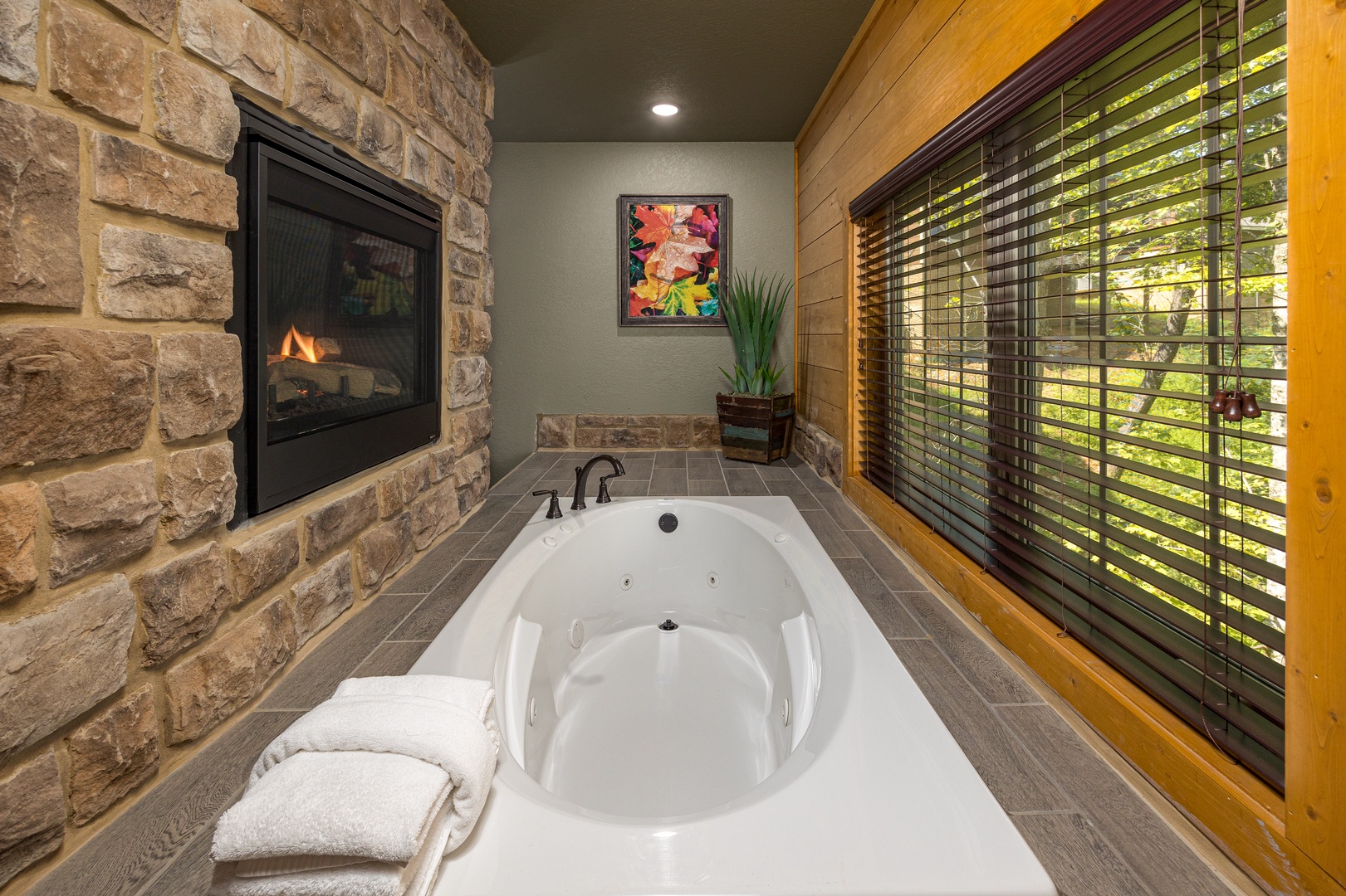 Southern Comfort spa bathroom, large round jetted soaking tub, stone fireplace, wood-panel accent wall, and garden window at Laurel Estates