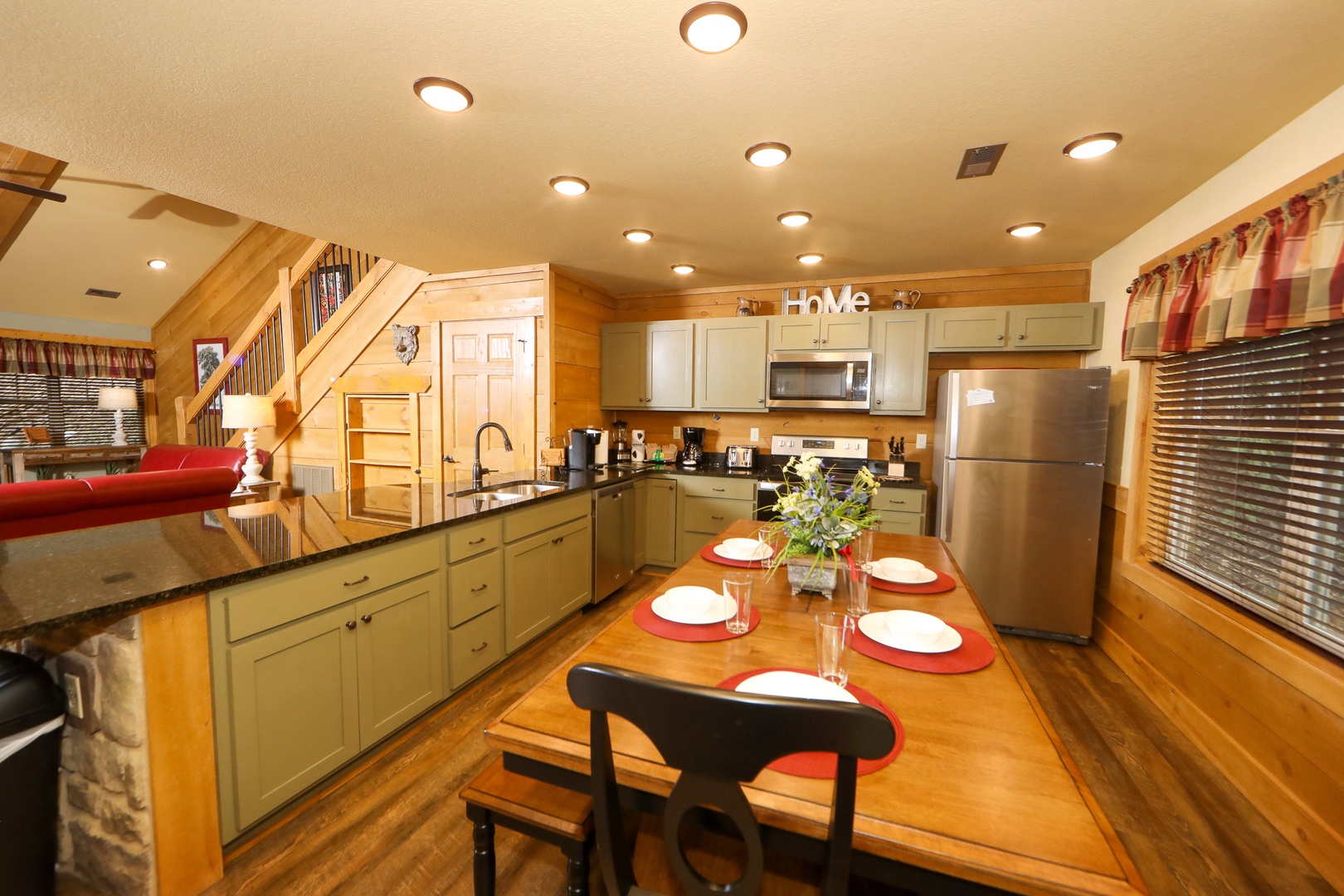 Ivie Holler open kitchen, sage green cabinetry, granite countertops, stainless appliances, and farmhouse dining table at Laurel Estates