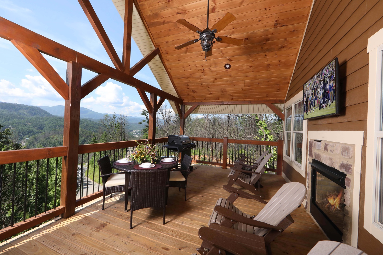 Above It All covered outdoor deck, panoramic Smoky Mountain views, stone outdoor fireplace, dining area, Adirondack chairs, and outdoor TV at Laurel Estates
